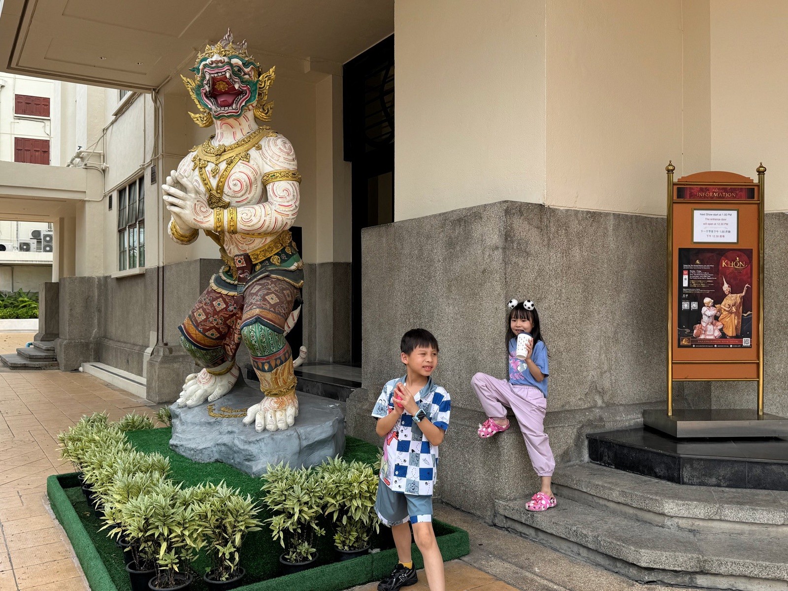 Children beside a traditional guardian figure outside Sala Chalermkrung